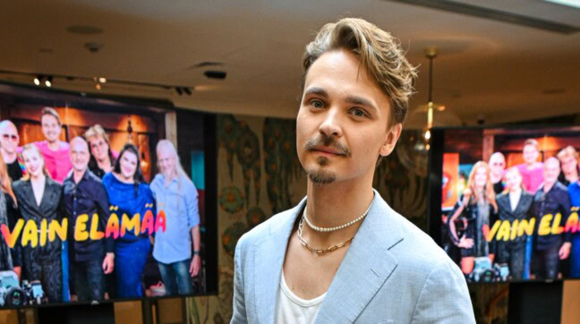 Roope Salminen kuvassa taustallaan televisioscreenejä joissa näkyy vain elämää -ohjelman artisteja